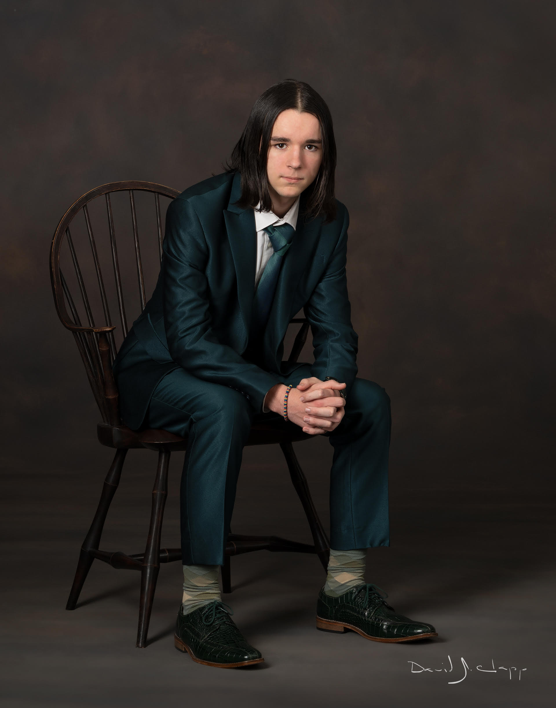 Benjamin Mark Ewing 2, seated in a wooden Windsor chair, wearing a deep green suit.